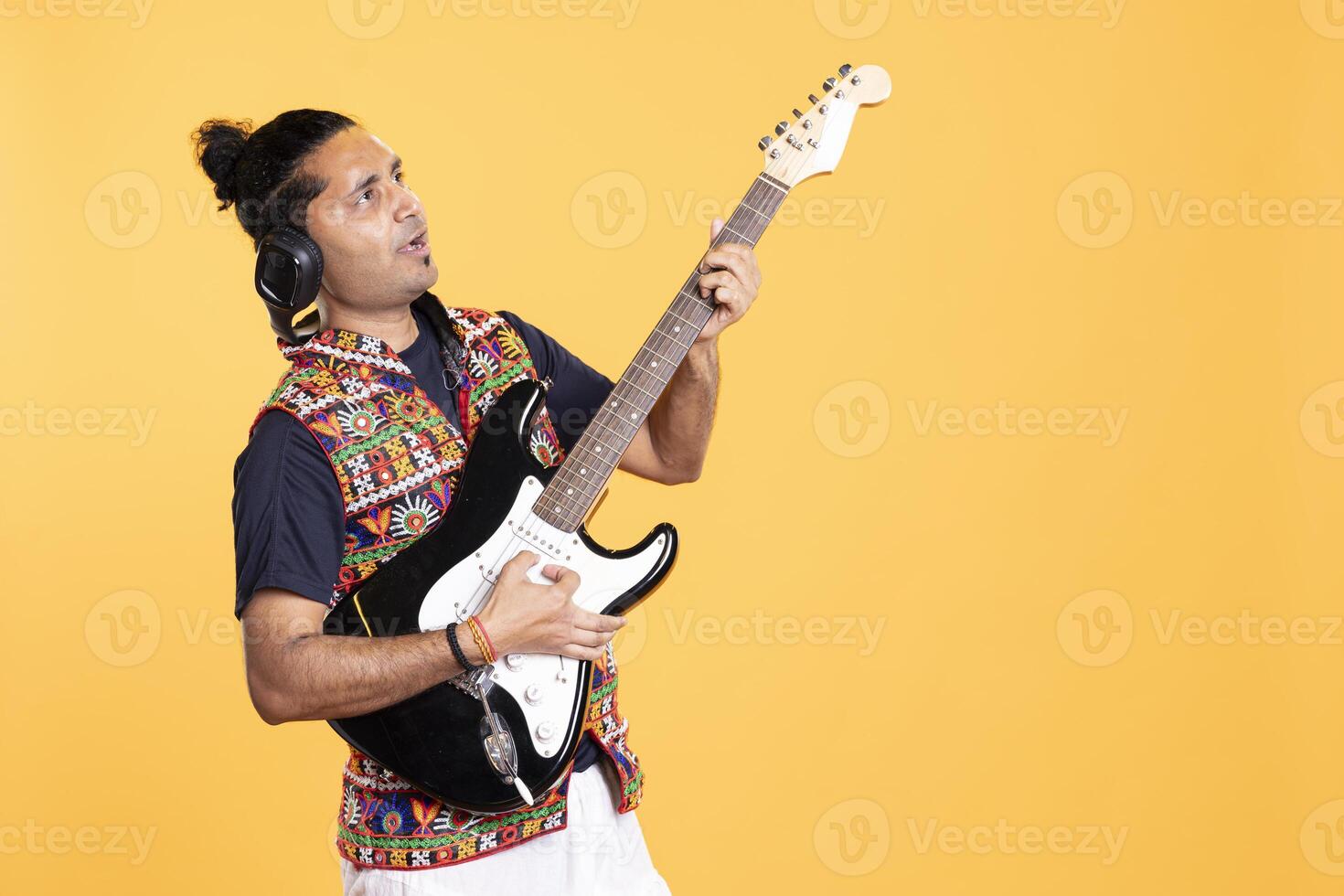 Talented person playing rock music with electric guitar, isolated over studio backdrop. Indian musician using musical instrument, having fun doing concert, producing entertaining songs photo
