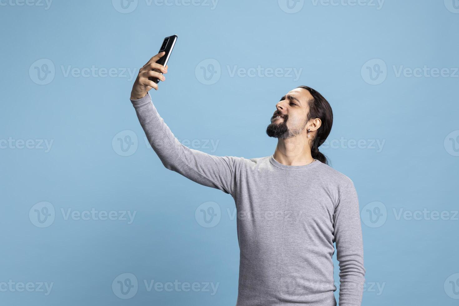 Male person discussing and laughing with his friends by conferencing, using online network on a call against blue background. Young joyful adult enjoying web discussion. photo