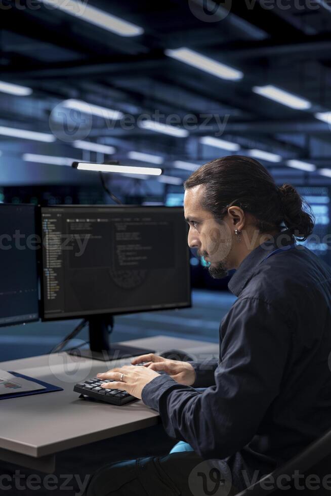 Admin typing on desktop PC in server farm establishment, ensuring data remains shielded from potential threats. IT specialist coding at computer desk, safeguarding data center against malicious access photo