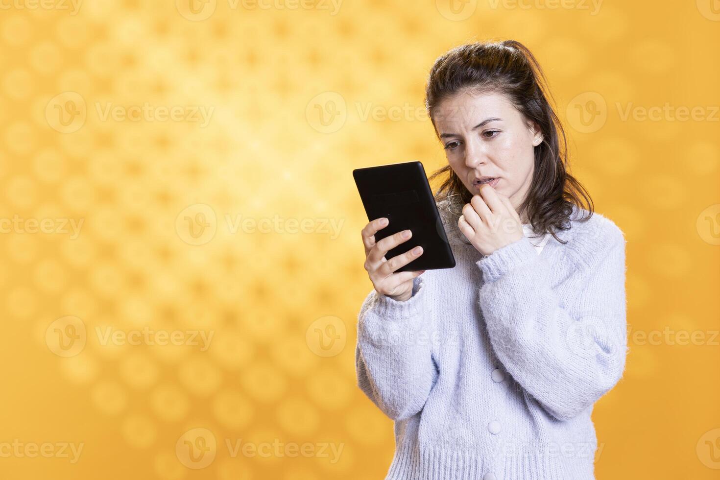 Woman reading ebook on ereader, rubbing lips, captivated by plot, enjoying hobby during leisure time. Lady with tablet in hands enchanted by enthralling digital novel story, studio background photo