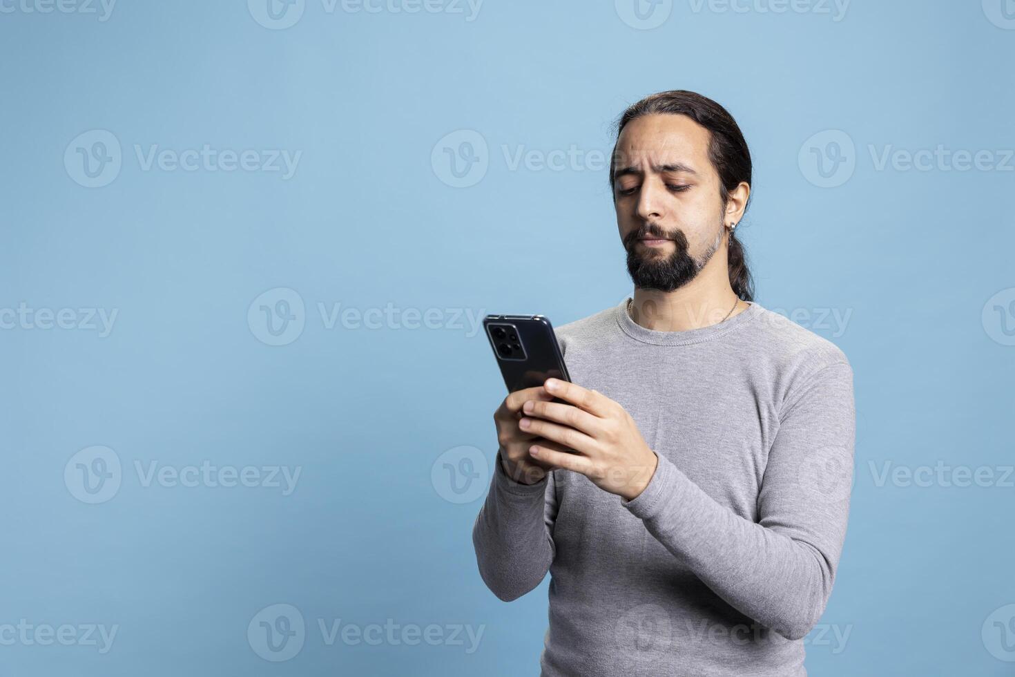Tech savvy individual holding a phone against a blue background, conveying calm and professionalism. Cool natural guy illustrating online work, digital engagement or networking in the digital world. photo