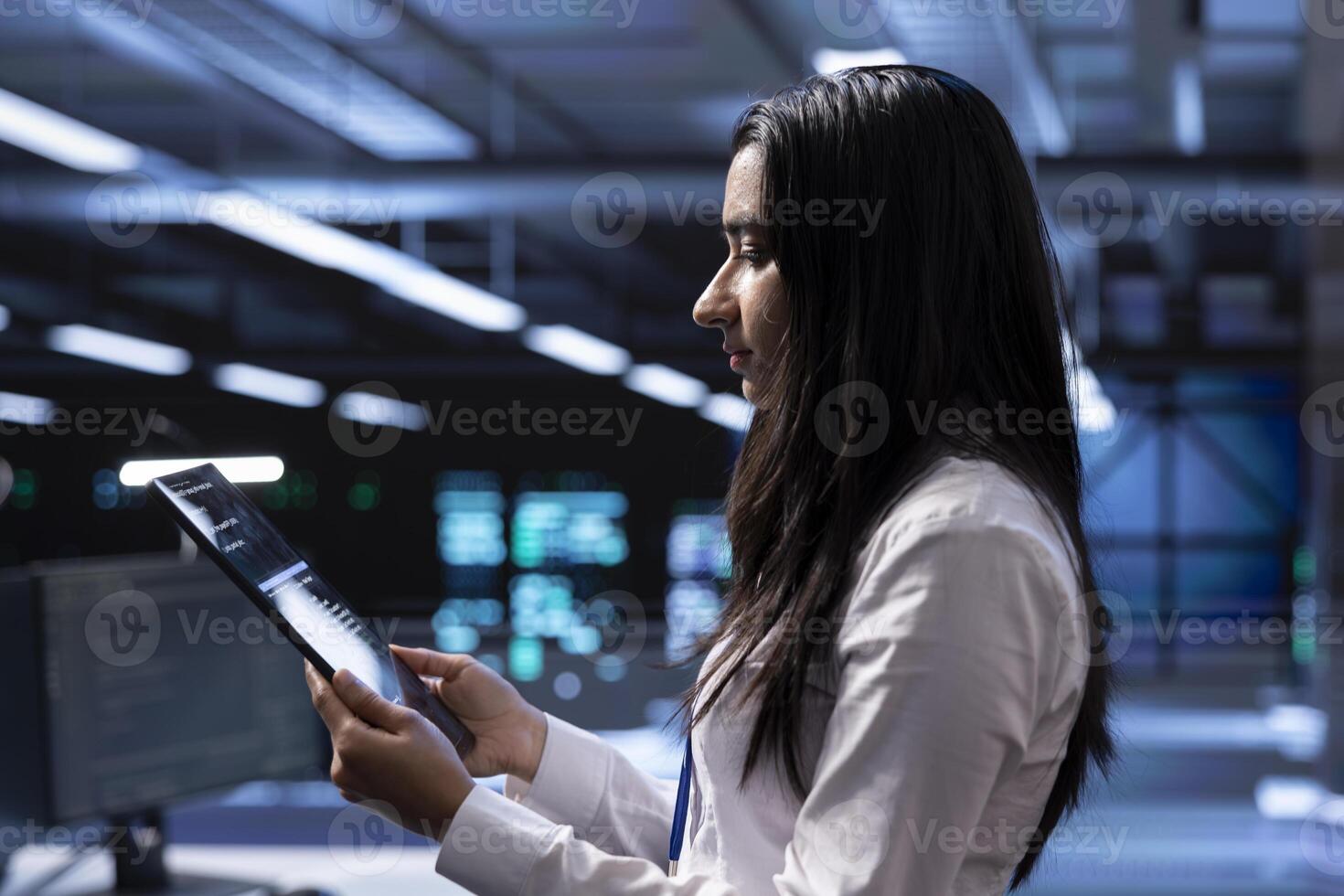 Engineer in data center updating systems to keeps performance up and protect servers from easily exploitable software vulnerabilities. Employee looking for errors causing servers to slow down using tablet photo