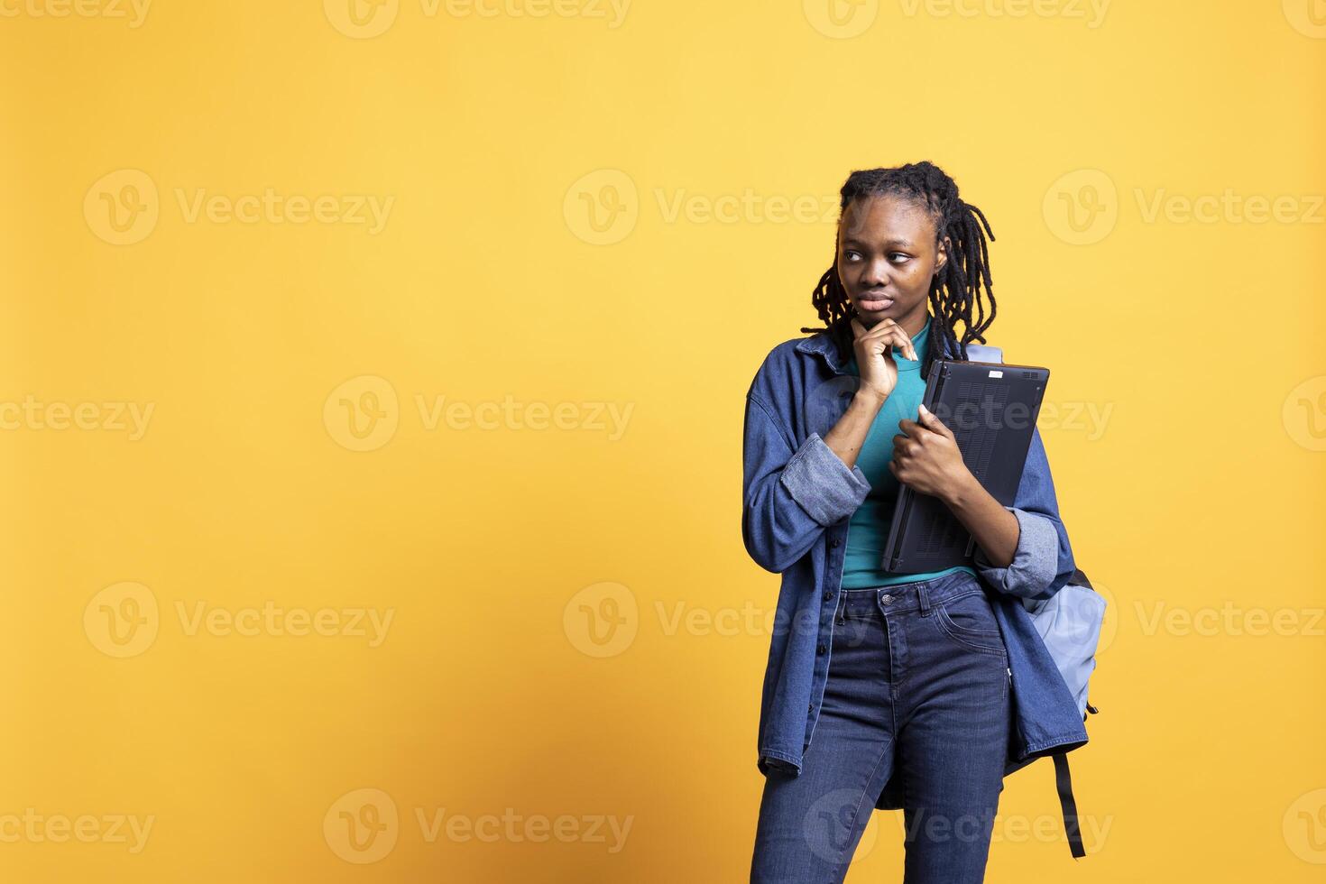 Pensive woman carrying laptop, using it to memorize information for school exam, studio background. Student holding notebook, remembering and practicing before university assessment photo
