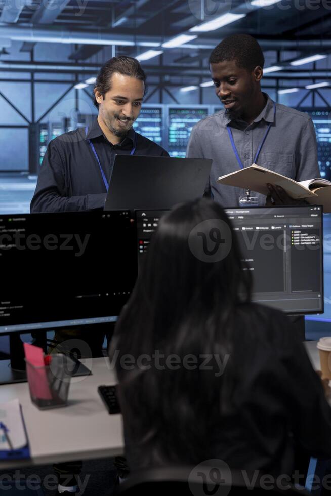Cheerful teamworking engineers in data center looking for firewall misconfigurations affecting servers. Happy multiethnic employees checking systems bottlenecks leading to sluggish data transfer rates photo