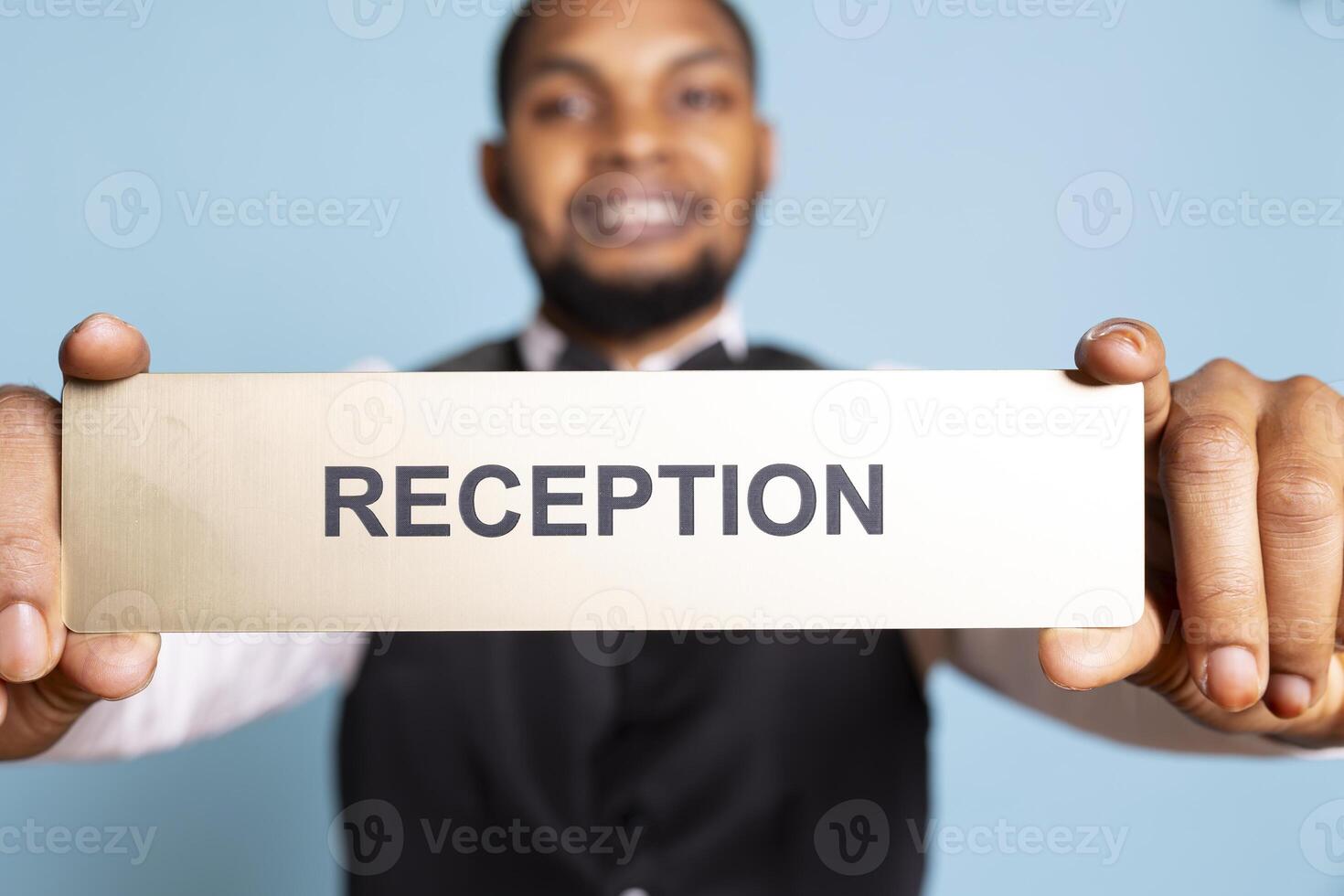 Young bellhop pointing at an indicator for the reception area front desk, working at a five star hotel and guiding clients to all the resort amenities. Bellboy doorkeeper with suit and tie. photo