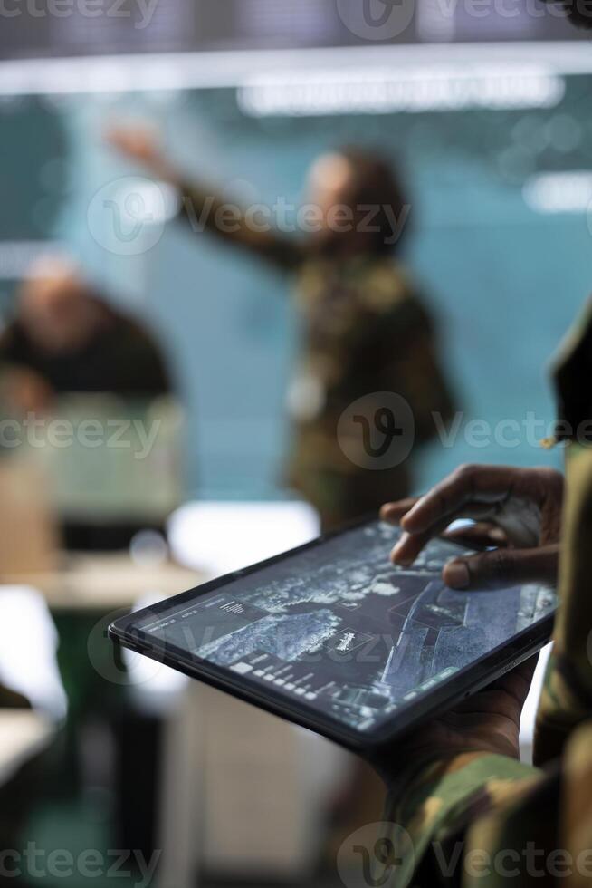 Army staff monitoring infantry unit on ongoing operation using his tablet, using surveillance radar system and a world map. IT professional working with reconnaissance gear. Close up. photo