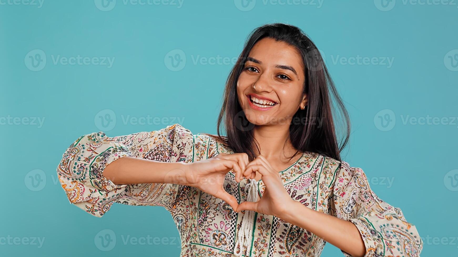 Portrait of smiling loving woman doing heart symbol shape gesture with hands, showing kindness. Happy affectionate girlfriend doing tender love gesturing for boyfriend, studio background, camera B photo