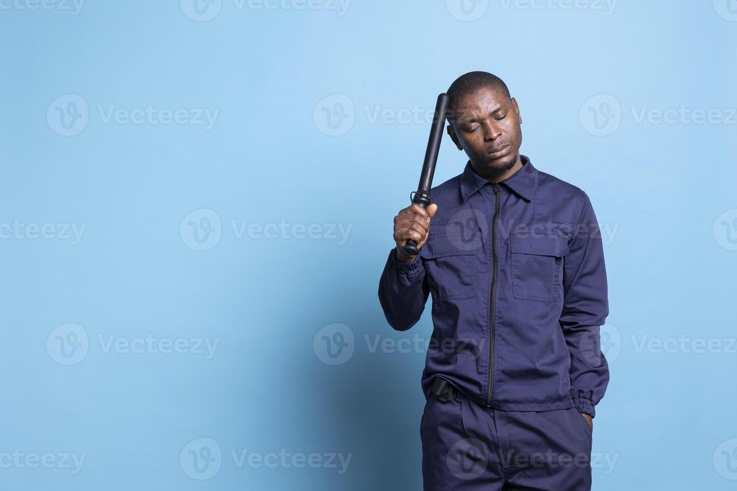 Portrait of african american security guard relaying on his baton weapon in case of emergency for defending and protection. Male agent skilled in combat, feeling confident in his abilities. photo