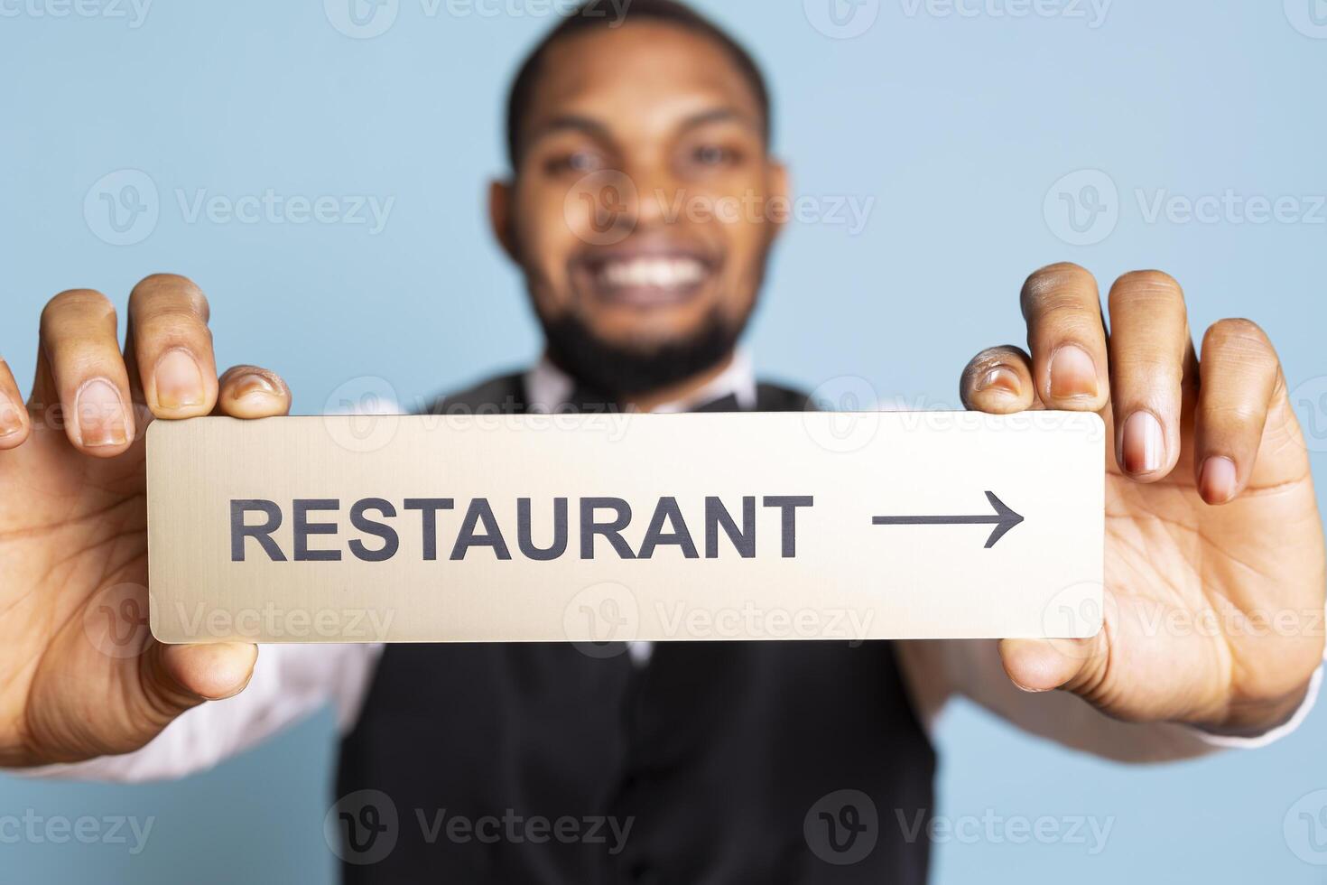 Hotel porter presenting the direction to the restaurant with a pointer, holding an indicator to guide clients to the amenities. Professional staff in tuxedo using a wall sign. Close up. photo