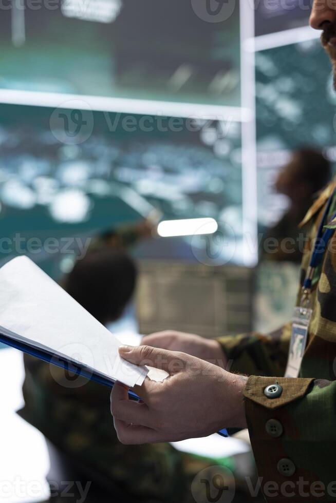 Soldier examining top secret operation details from the case file, going over important battlefield data to ensure defense mission success. Trooper operating in command post. Close up. photo