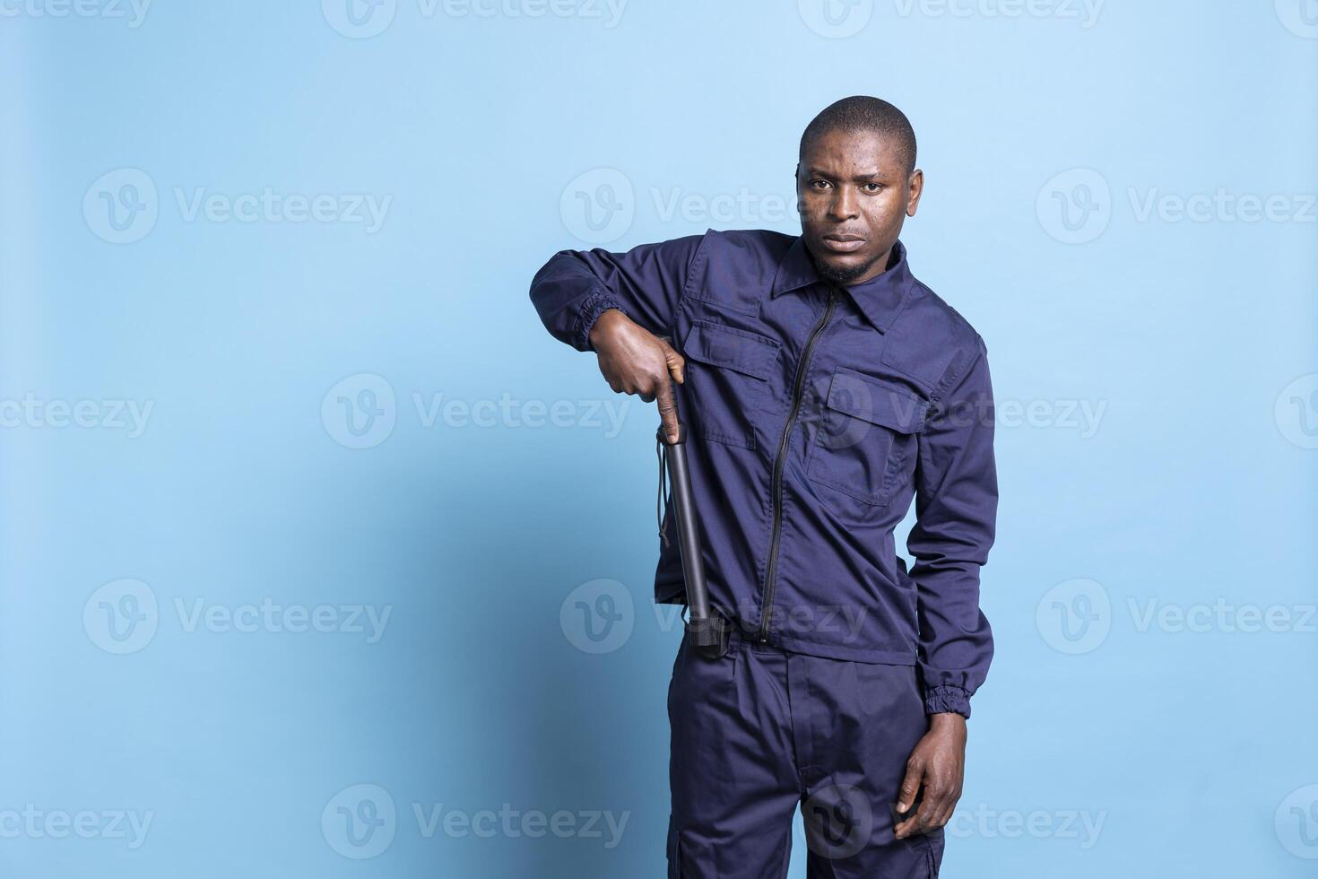 Security guard on duty taking out his weapon against blue background, preparing for a fight. Armed officer in uniform carrying his baton and getting ready for an emergency defense. photo