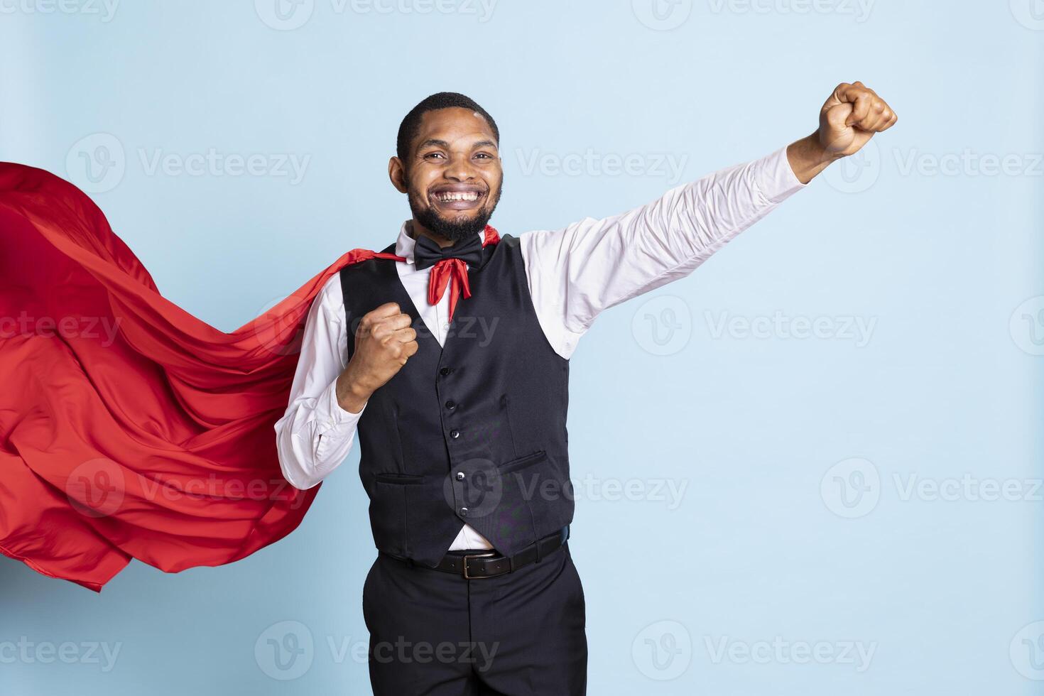 African american doorman posing in a superhero red mantle in studio, acting as a hero and savior for the clients. Happy confident bellhop with a superhuman cape, professionalism. photo