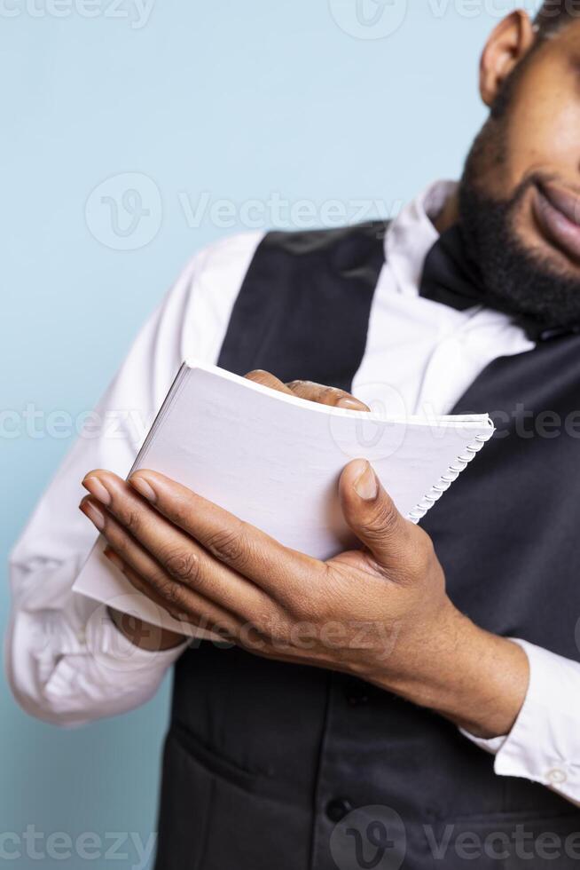 Hotel porter bellhop writes guests requests on smartphone call, discussing about amenities included in the room price. Doorkeeper staff takes notes with a list of guests in the ledger. photo