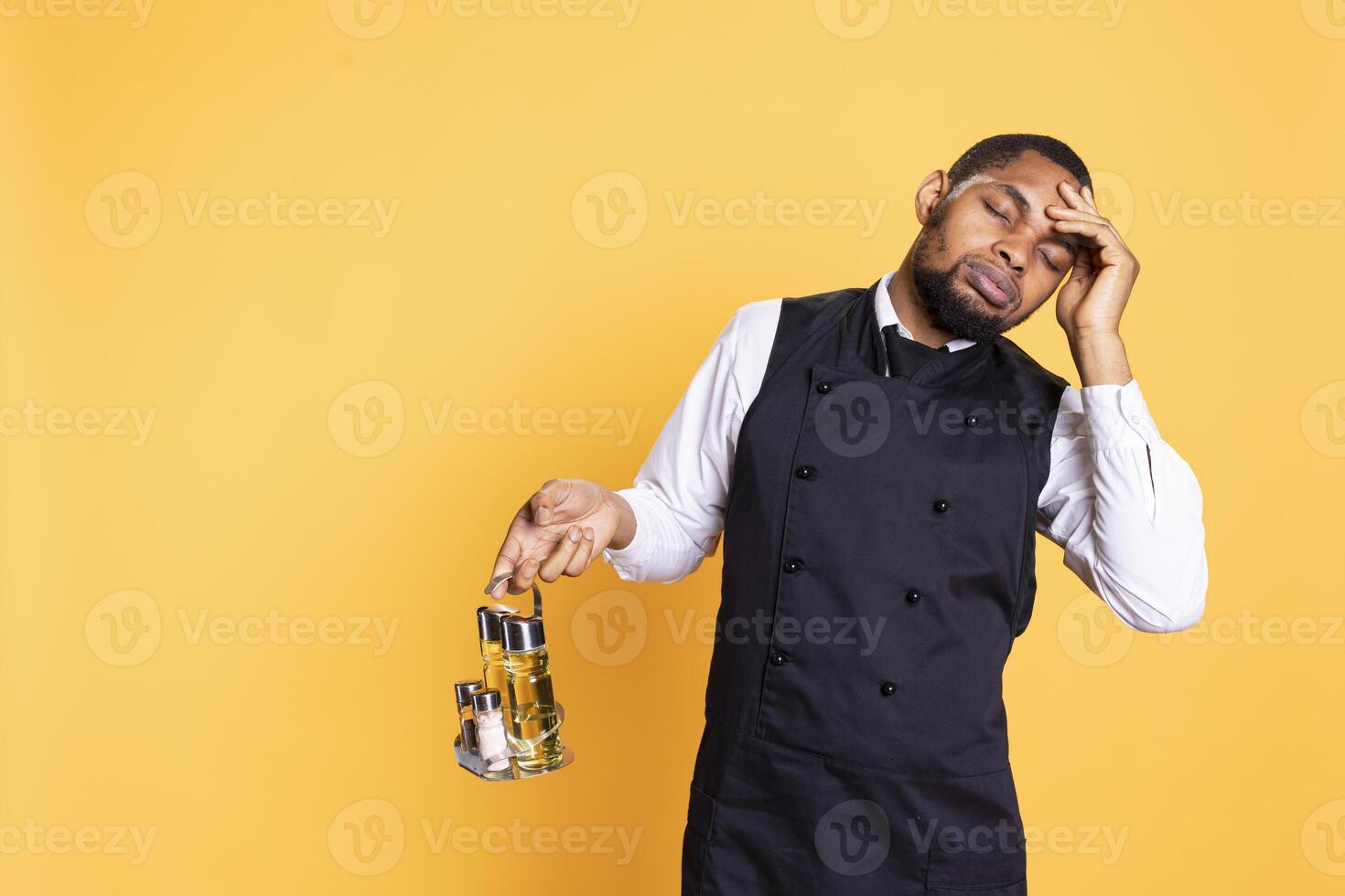 Restaurant butler working on serving clients with a headache, feeling tired and overworked in service oriented industry. Young caterer suffering from a painful migraine in studio. photo