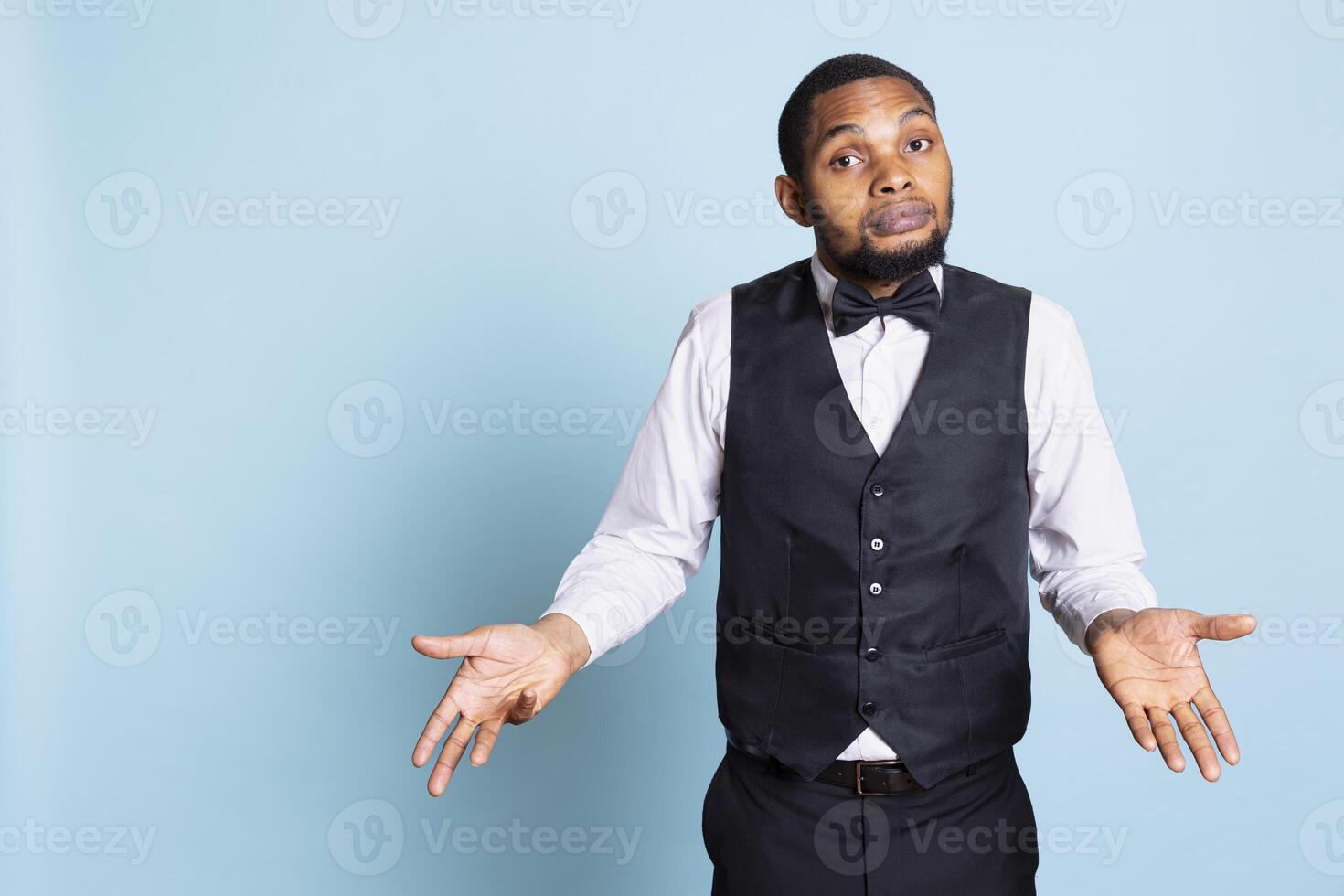 Undecided confused hotel concierge with suit and tie shrugging on camera, showing uncertainty with i dont know gesture. Clueless hotelier staff acting unsure and puzzled, confusion. photo