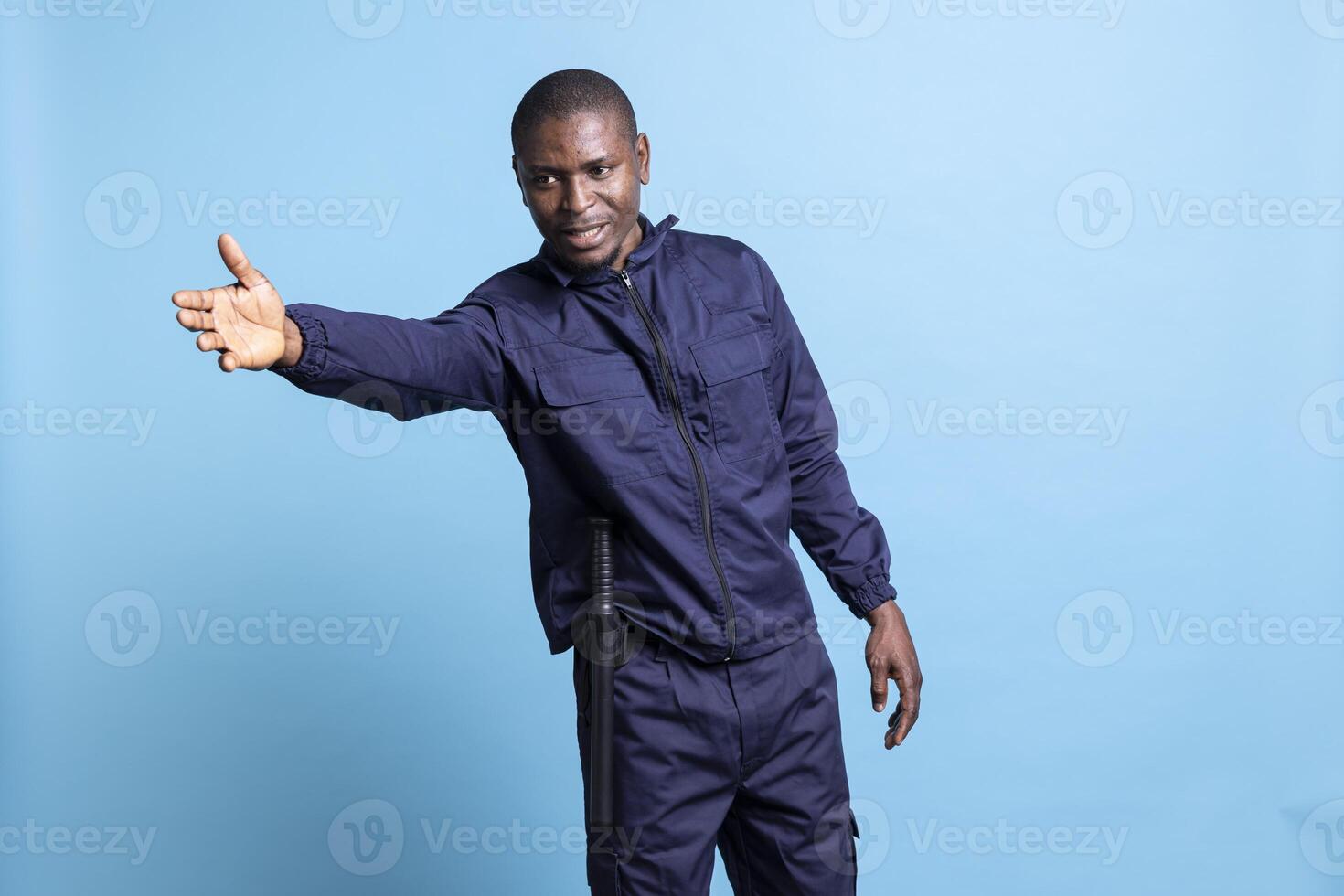 African american guy works as a security guard in front of the camera, restricting the access and pointing persons in another direction. Patrol officer is guiding people to left or right in studio. photo
