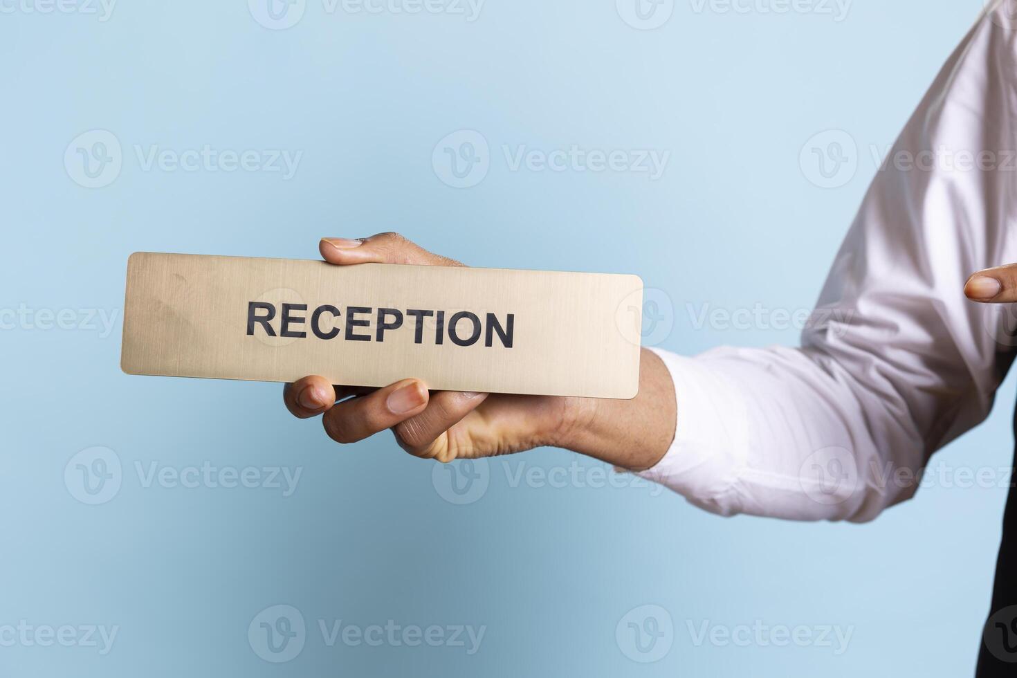 Young bellhop pointing at an indicator for the reception area front desk, working at a five star hotel and guiding clients to all the resort amenities. Bellboy doorkeeper with suit and tie. photo