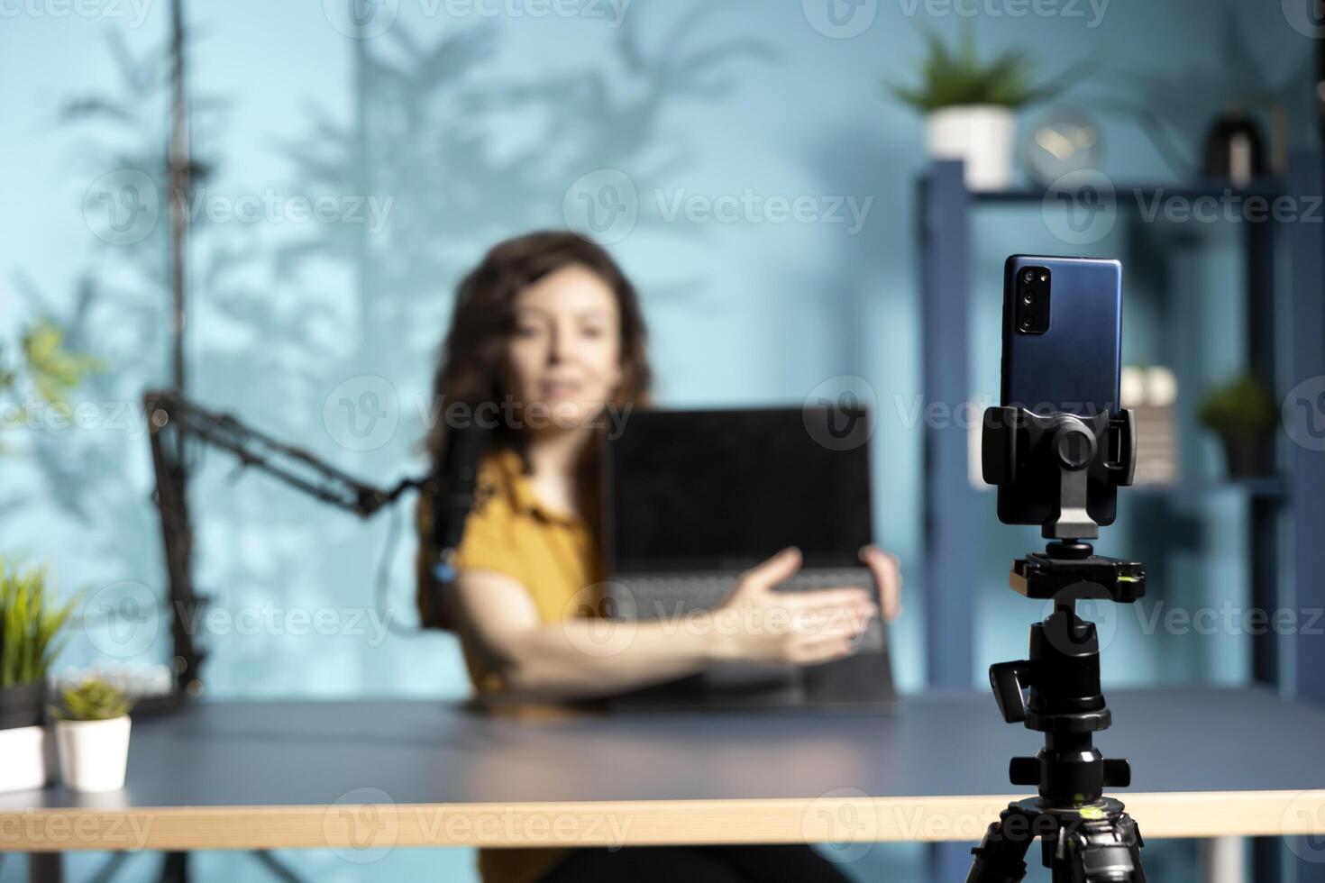 Focus on smartphone used by woman in studio to film laptop from brand sponsoring , talking in microphone. Close up of phone used by content creator to do influencer marketing, promoting notebook photo