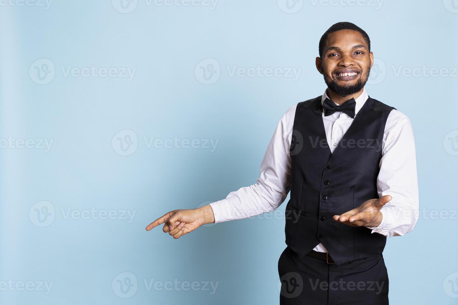 Doorman staff pointing at something to left or right sides in studio, indicating the direction for some amenities at the five star hotel. Bellboy porter wearing a suit and tie uniform on duty. photo