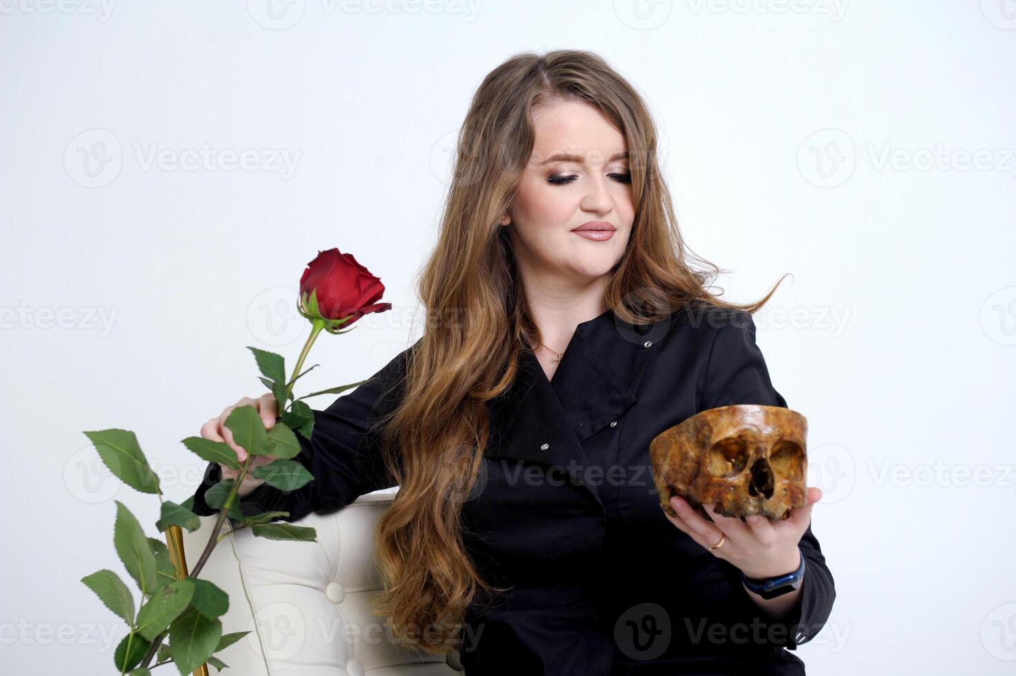 Woman posing with red rose in graveyard scene while wearing skeleton makeup to celebrate dios de los muertos. Macabre lady dressed as La Catrina character on day of the dead event in misty studio photo