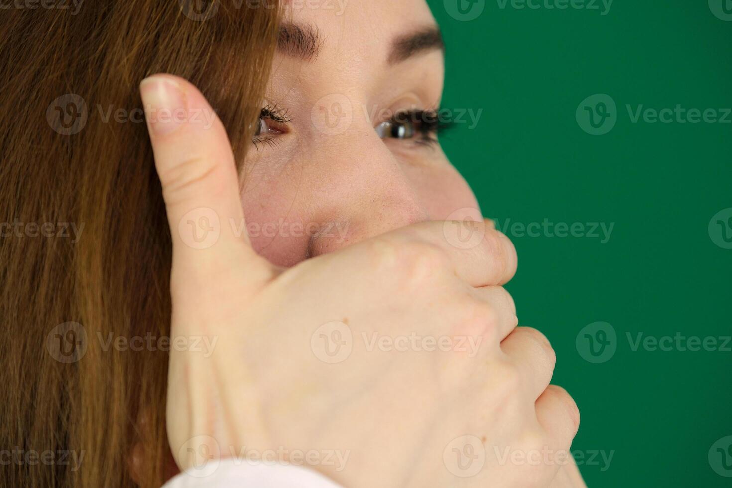 Surprised caucasian girl covering her mouth and looking at camera isolated over green background photo