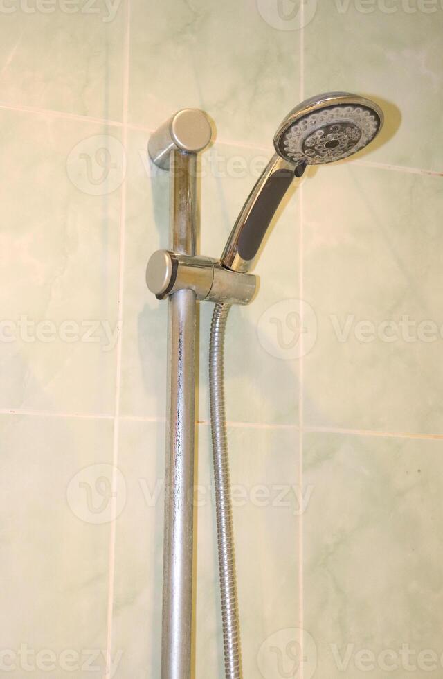 Shower head with hose with limescale deposits in holder on wall in bathroom photo