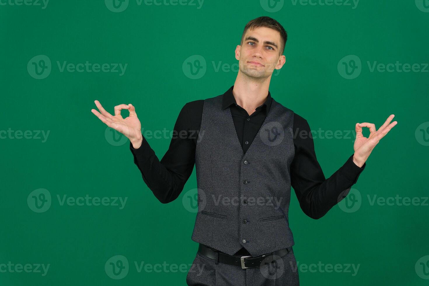 young businessman feeling successful and satisfied, smiling with mouth wide open, making okay sign with hand against green background photo