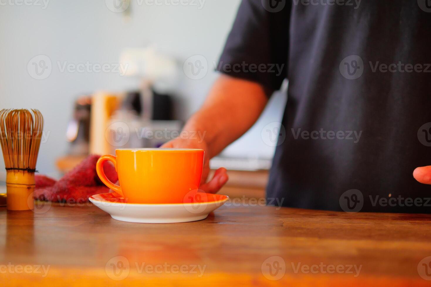 Carefully and intentionally placing a vibrant orange cup on a wooden table photo