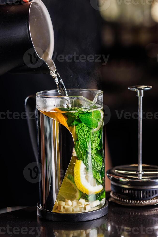vitamin tonic tea with lemon, ginger and mint, on a dark background in a transparent teapot photo
