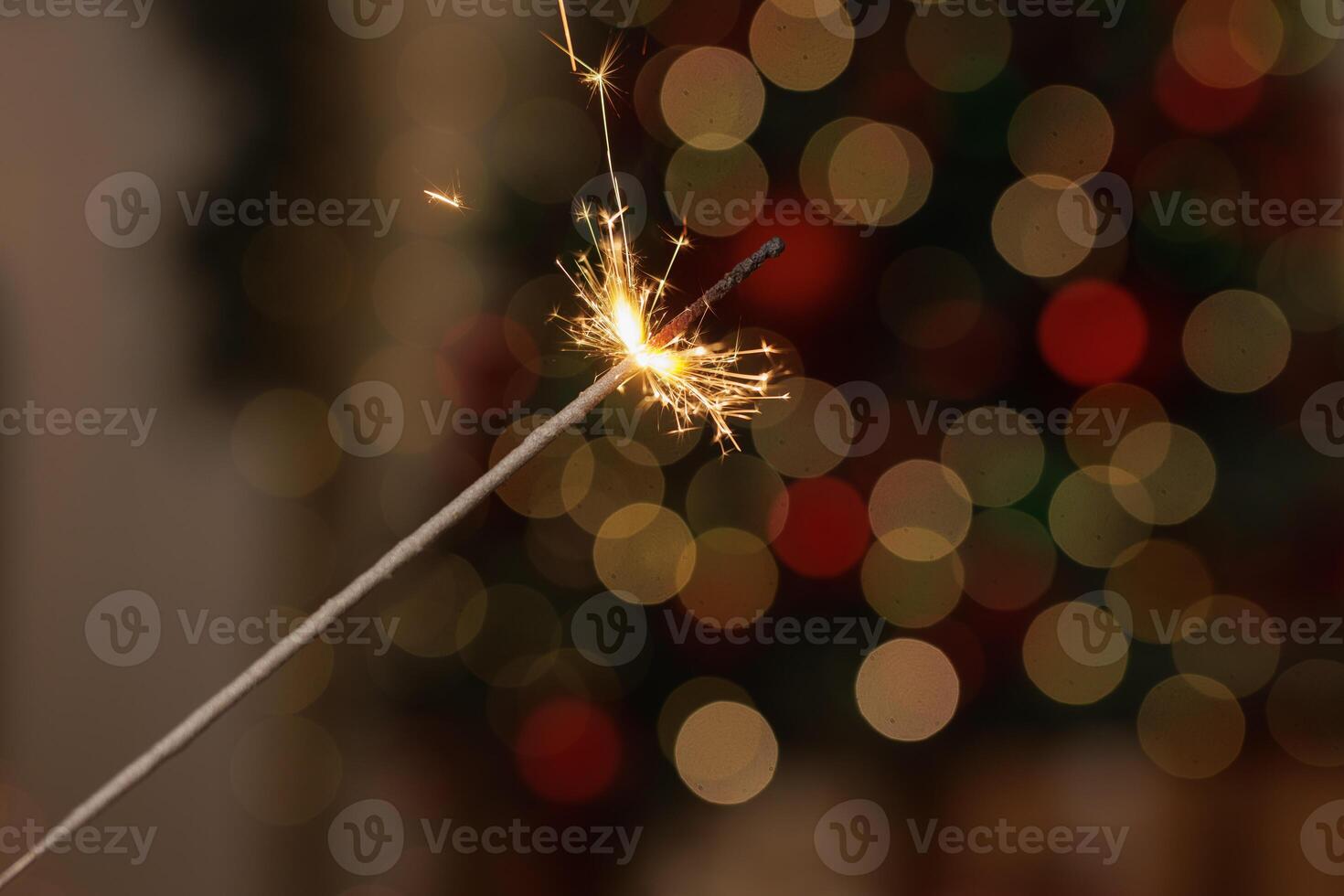 Burning sparkler in female hand on background of christmas tree lights in dark room photo