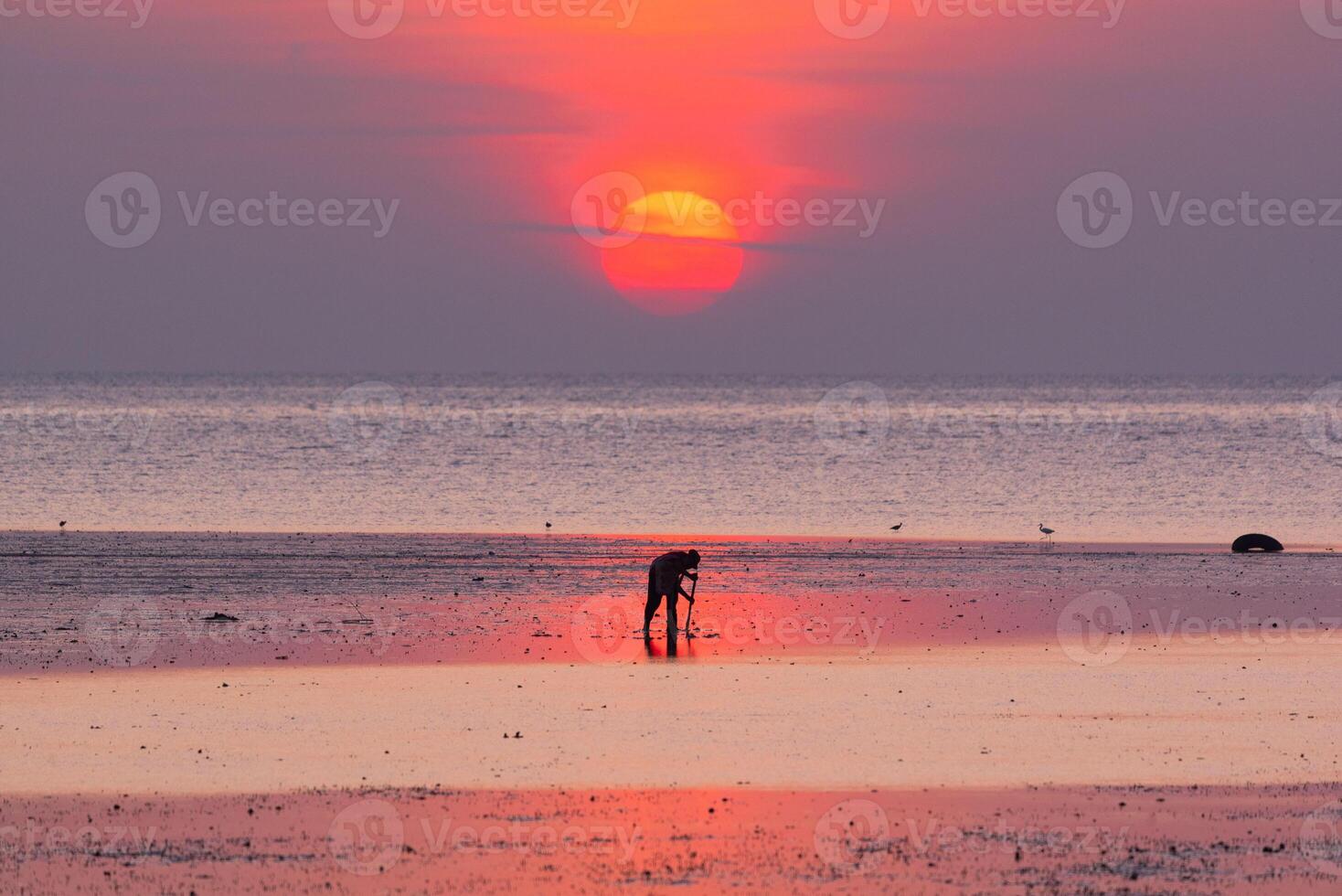 Silhouette of a fisherman against a calm sea during sunrise at Phuket city photo