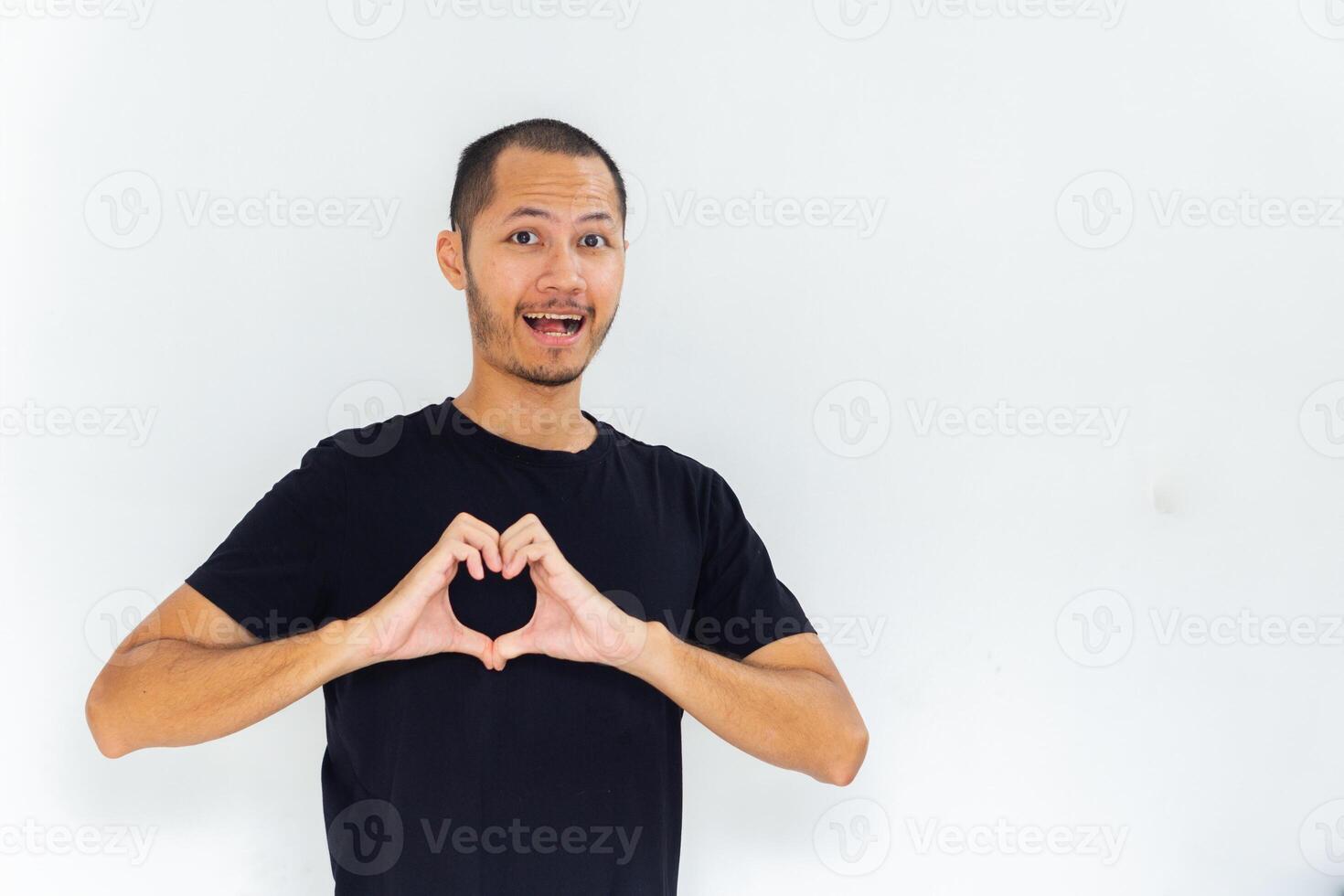 Young man wearing empty black shirt showing heart sign with hand on chest with isolated white background photo