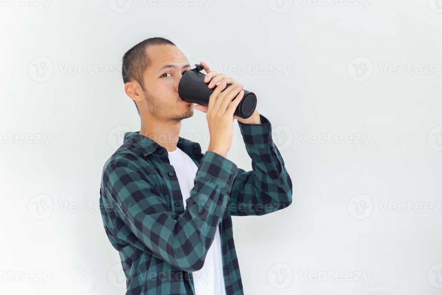 Young asian men wearing flannel and shirt is drinking from black tumbler with smile in isolated white background photo