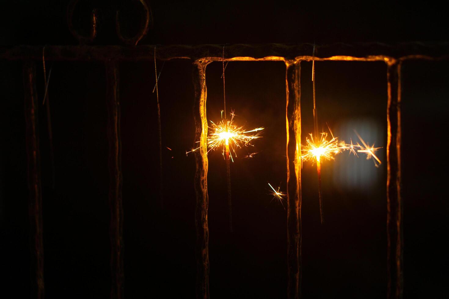 Two firework sparkles are hanging on fence in night with blurry background for new year event photo