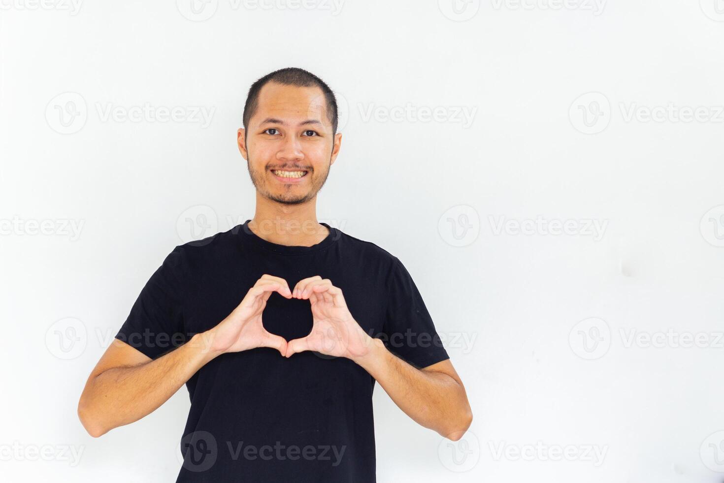 Young man wearing empty black shirt showing heart sign with hand on chest with isolated white background photo