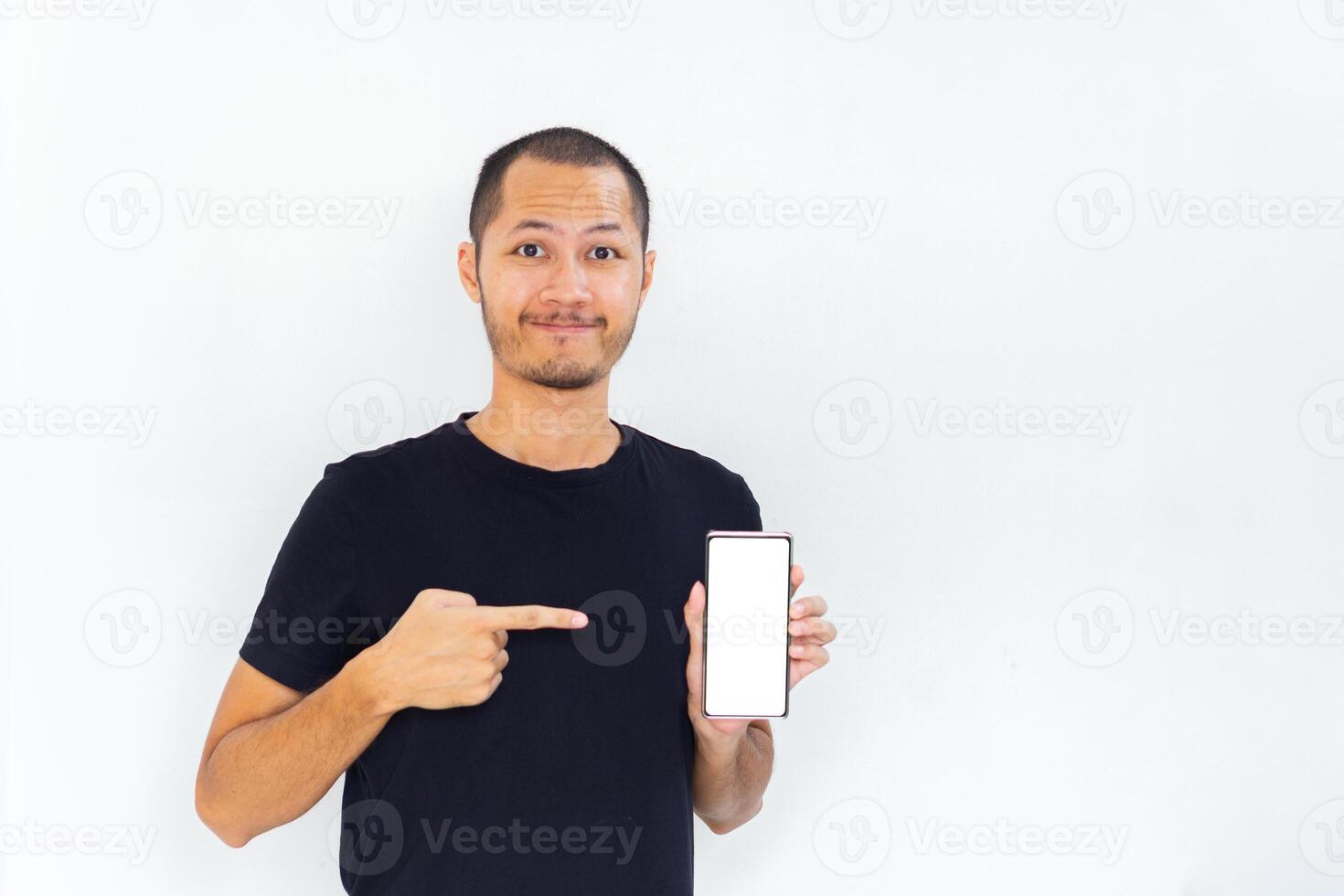 Young men with black empty shirt smiling and pointing to phone with white screen template mockup photo