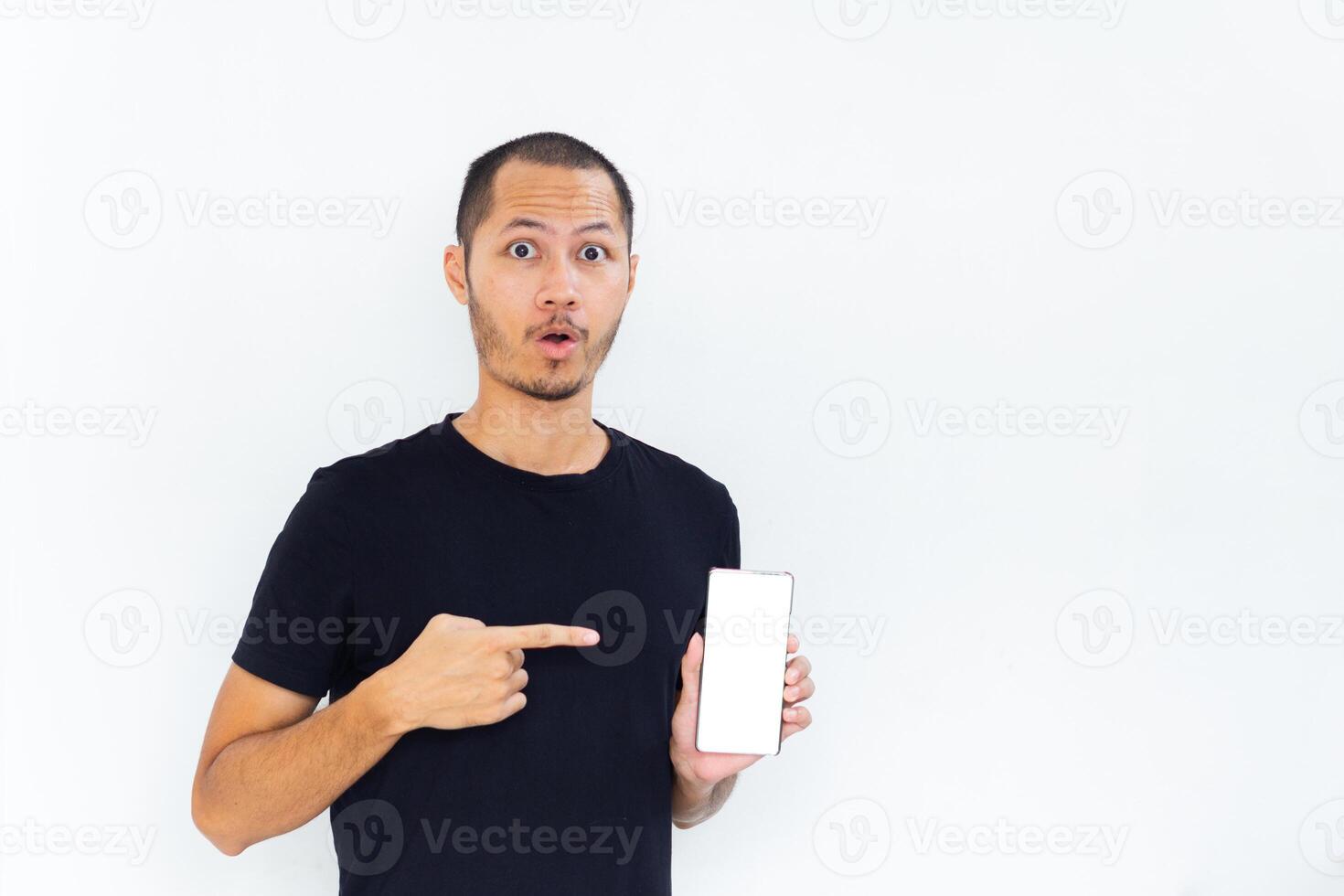 Young men with black empty shirt smiling and pointing to phone with white screen template mockup photo