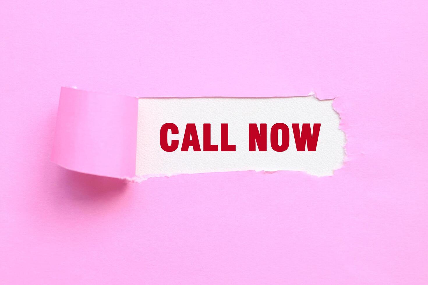 Call now message written on ripped torn pink paper. CALL NOW text photo