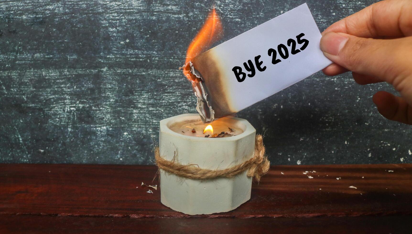 Hand holding a half-burnt note with Bye 2024 written on it on the candle. Burn the past 2024. Say goodbye to 2024. photo