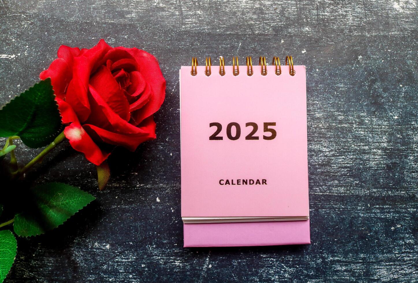 2025 calendar in pink and red roses on the table. Calendar and Note Pad Happy New year 2025. 2025 New Year resolutions goal, plan, and action concept photo