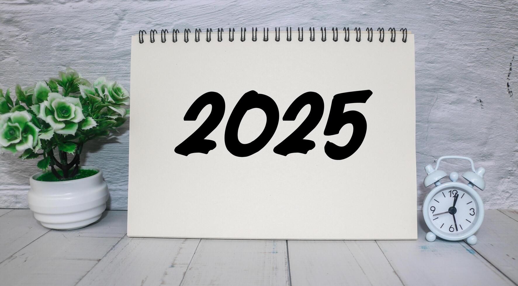 A workspace featuring a notepad with 2025 happy new year. Notebook on the table with the year 2025 written on it. photo