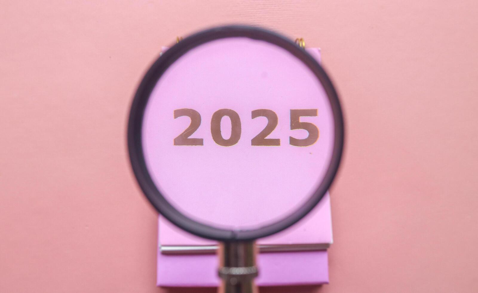 Magnifying glass in 2025 Calendar in pink isolated on pink background. Calendar and Note Pad Happy New year 2025. 2025 New Year resolutions goal, plan, and action concept photo