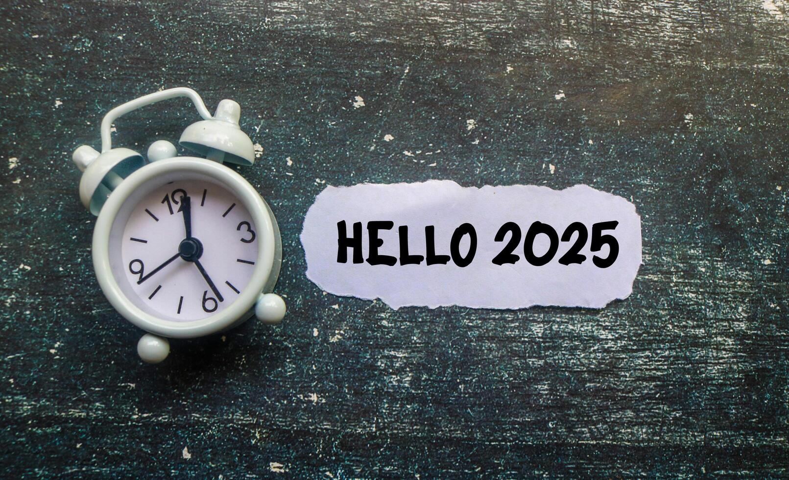 A paper cutout with Hello 2025 written on it is surrounded by a clock on the table. New Year 2025 concept, welcoming the new year 2025 photo