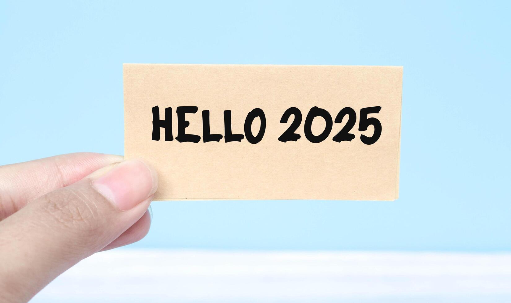 Hand holding note Hello 2025 isolated blue background. New year concept with typographic 2025. Motivational words to welcome the new year 2025 photo