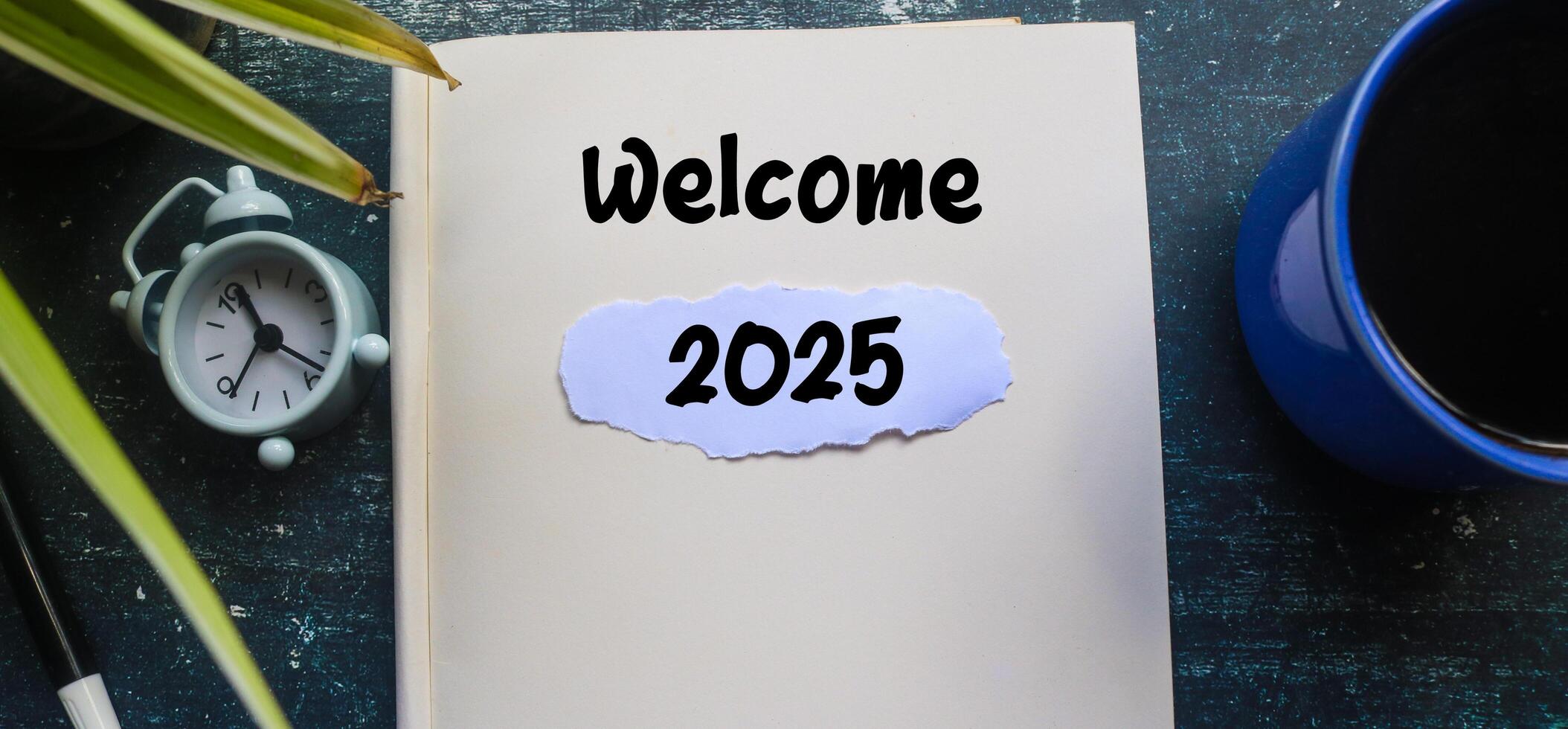 Welcome 2025 text on notebook with alarm clock on wooden table. Welcoming the new year 2025 photo