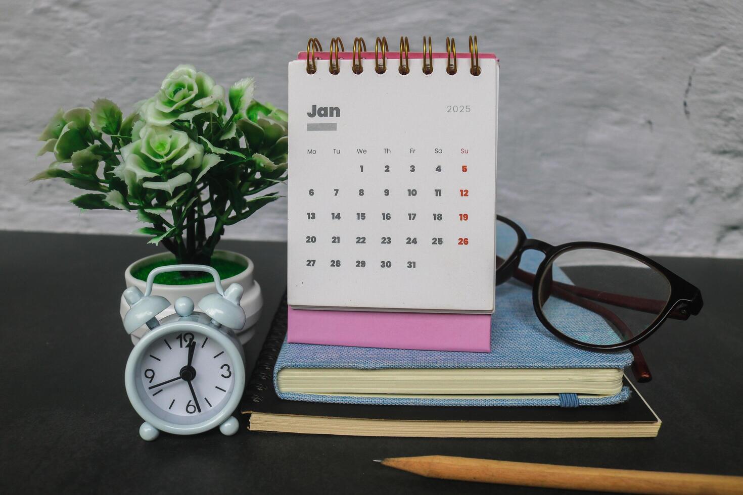The first month of January 2025 in the pink 2025 calendar on the office desk with a notebook and alarm clock. New year 2025 with office desk concept photo