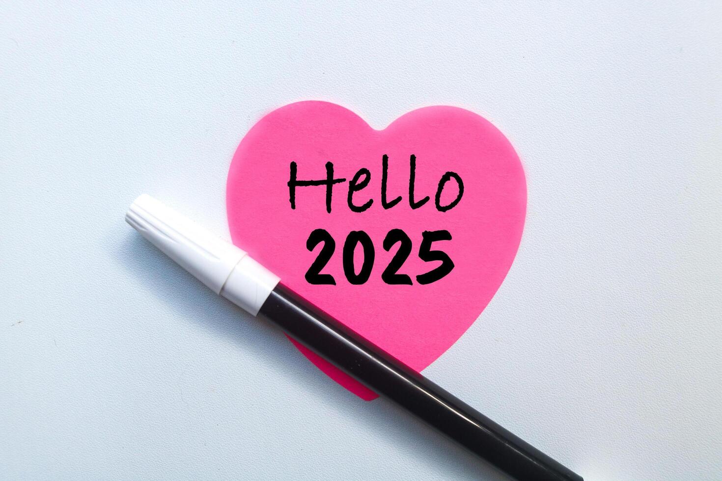 Pink love sticky note with Hello 2025 written on it with pen isolated on white background. Welcoming the new year 2025 concept photo