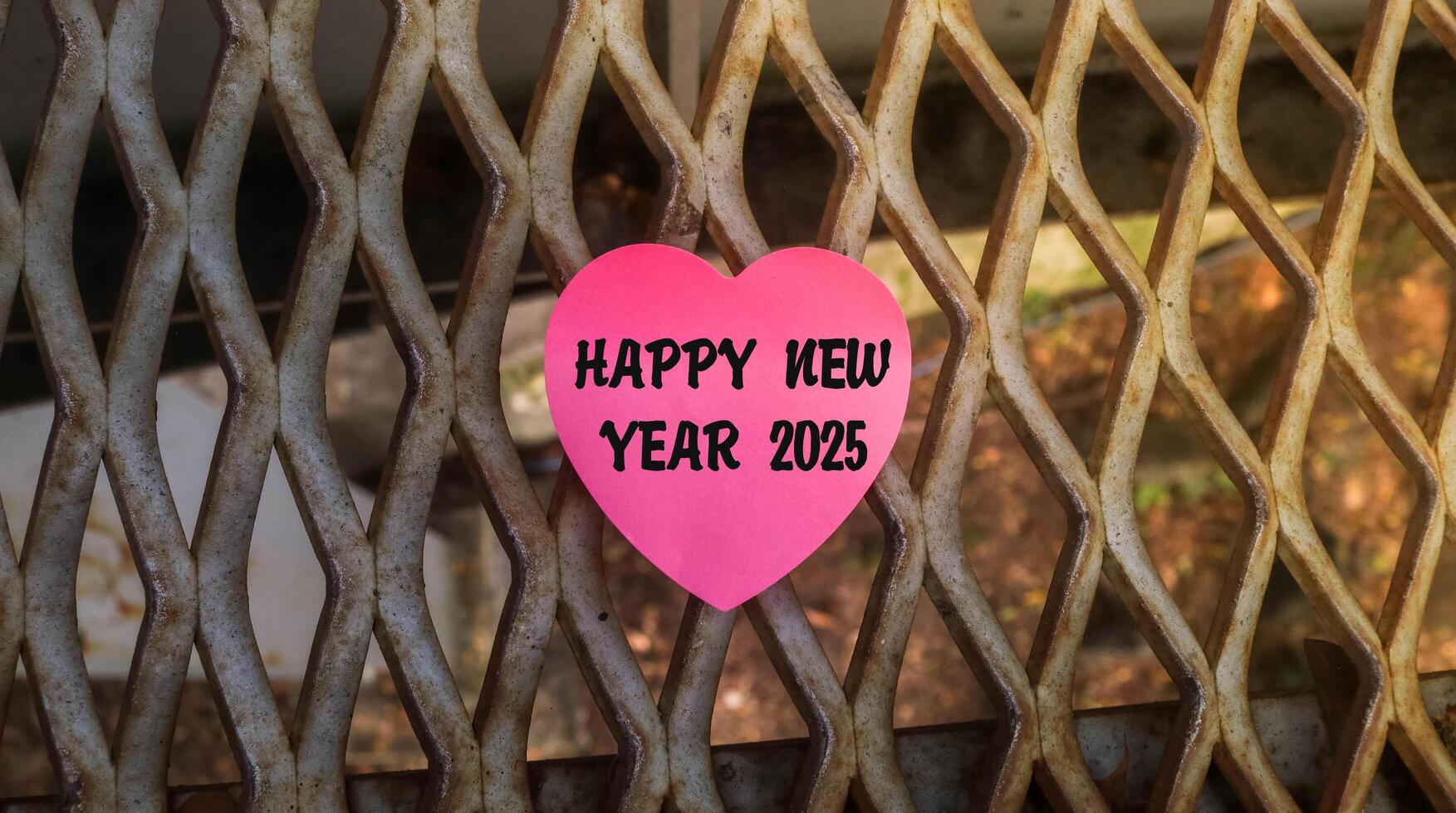Aesthetic pink love sticky note with Happy new year 2025 written on it. Welcome the new year 2025 concept with iron fence background photo