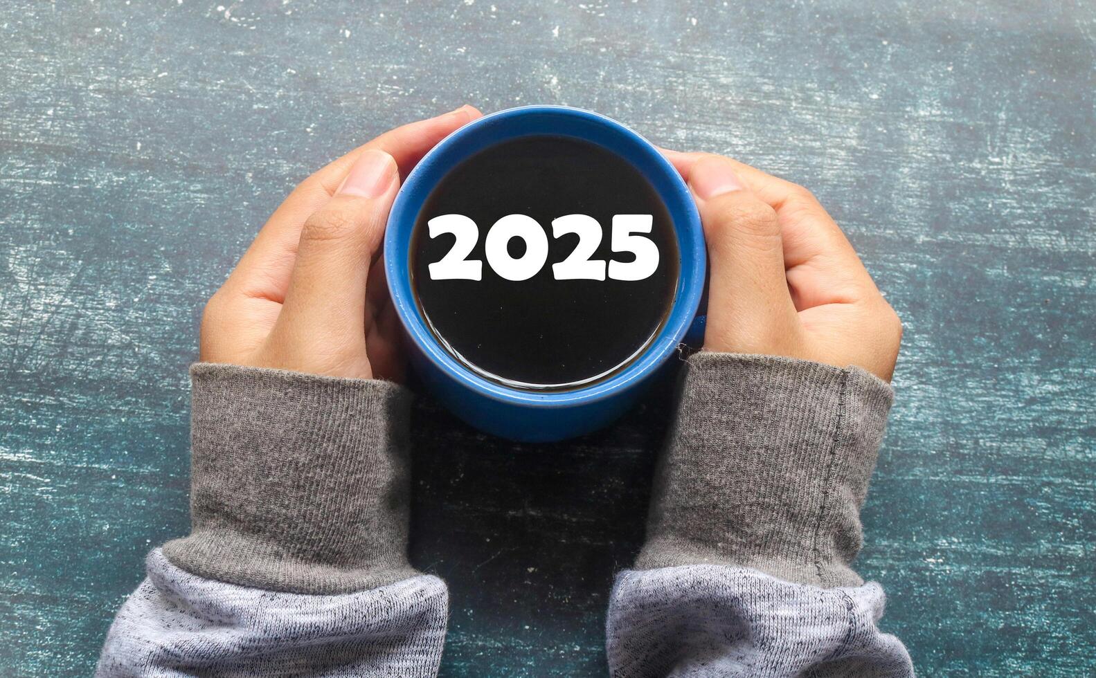 Hand holding a cup of black coffee with 2025 written on it. Top view of black coffee and New Year 2025 concept photo