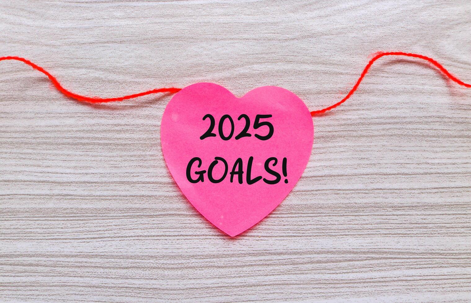 2025 Goals notes on pink heart shaped paper hanging on a string. New year concept with typographic 2025. Motivational words for the new year 2025 photo